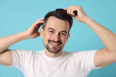 Yakışıklı adam saçlarını açık mavi arka planda tarak ile tarıyor.