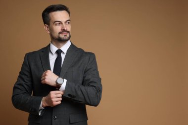 Kahverengi arka planda şık saati olan klasik takım elbiseli kendine güvenen bir adam. Metin için boşluk