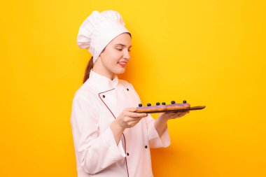 Üniformalı şekerci turuncu arka planda lezzetli ekinler tutuyor.