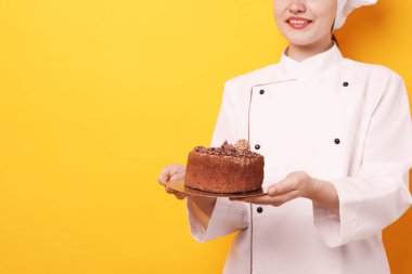 Üniformalı bir şekerci, turuncu arka planda çikolatalı kek tutuyor, yakın plan. Metin için boşluk
