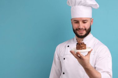 Üniformalı mutlu pastacı açık mavi arka planda çikolatalı tatlı tutuyor.