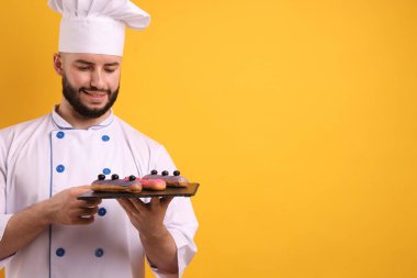 Üniformalı mutlu pastacı turuncu arka planda ekinler tutuyor, metin için yer var.