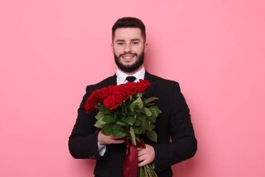 Pembe arka planda kırmızı güller açan mutlu bir adam.