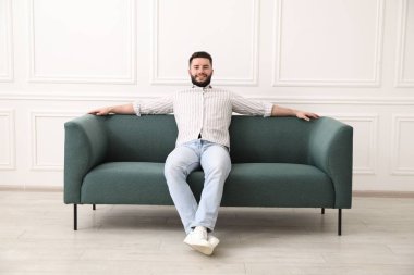 Evdeki kanepede dinlenen gülümseyen adam.