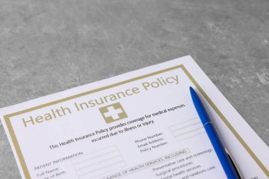 Sağlık sigortası formu ve kalem gri masaya, yakın plan.