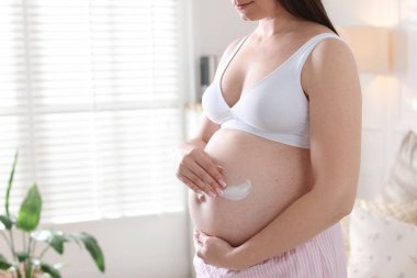 Evde karnına krem sürmüş hamile bir kadın, yakın plan. Metin için boşluk