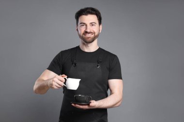 Gülümseyen barista gri arka planda kahve yapıyor.