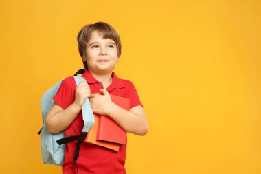 Turuncu arka planda kitapları ve sırt çantası olan küçük bir çocuk. Metin için boşluk
