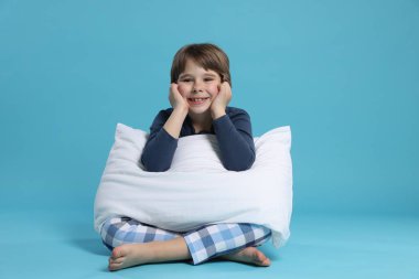 Açık mavi arka planda yastığı olan sevimli bir çocuk.