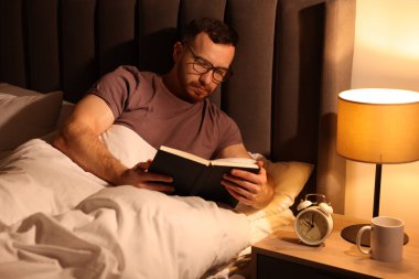 Genç adam evde yatakta kitap okumak