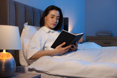 Evde yatakta kitap okuyan genç bir kadın.