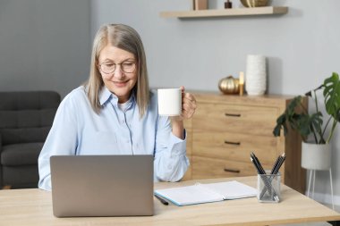 İçerideki masada bilgisayarla fincan öğrenen gülümseyen bir kadın. Kendi kendine çalışma.
