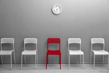 Farklı, eşsiz, özel. Gri duvarın yanındaki beyazların arasında kırmızı sandalye.