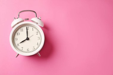 Pembe arka planda beyaz alarmlı saat, üst manzara. Metin için boşluk