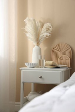 Yatağın yanında kitap, dekor ve bir bardak su olan komodin.