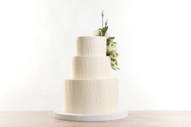 Ahşap masada çiçeklerle süslenmiş nefis düğün pastası beyaz arka planda.