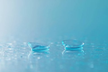 Açık mavi ayna yüzeyine bir çift kontak lens ve su damlası, yakın plan.