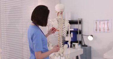 Doktor klinikteki insan iskeleti modelini işaret ediyor.