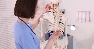 Doktor klinikteki insan iskeleti modelini işaret ediyor.
