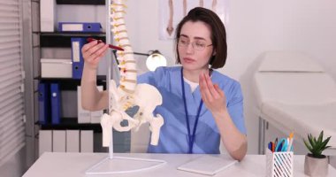 Doktor, klinikteki masadaki insan omurga modeline işaret ediyor.