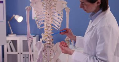 Doktor klinikteki insan iskeleti modelini işaret ediyor.