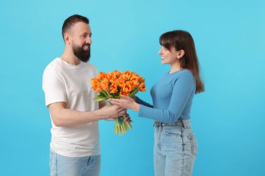 Bir adam açık mavi arka planda sevgili karısına güzel laleler sunuyor.