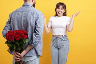 Adam turuncu arka planda sevgilisine kırmızı gül buketi saklıyor.