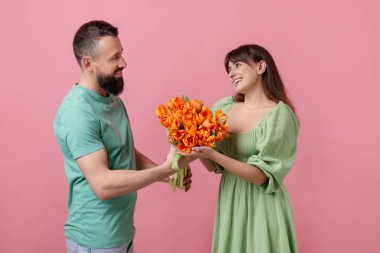 Adam pembe arka planda sevgili karısına bir buket güzel lale sunuyor.