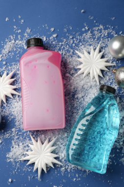 Plastik şişelerde antifriz, takılar, dekoratif kar taneleri ve mavi arka planda buz, düz bir zemin.