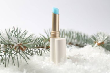 Nemlendirici dudak kremi ve suni kar üzerindeki köknar ağacı dalları beyaz arka planda, yakın plan. Kış bakımı