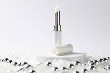 Nemlendirici dudak kremi ve yapay kar üzerindeki Noel süsü beyaz arka planda, yakın plan. Kış bakımı