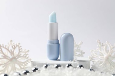 Nemlendirici dudak kremi ve yapay kar üzerindeki Noel süsü beyaz arka planda, yakın plan. Kış bakımı