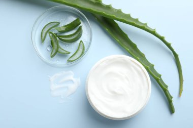 Aloe vera özütüyle nemlendirici krem ve açık mavi arkaplanda yapraklar, düz bir zemin.