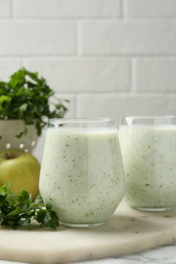 Sağlıklı maydanoz bardakta içer, yapraklar ve elmalar beyaz mermer masada, yakın plan