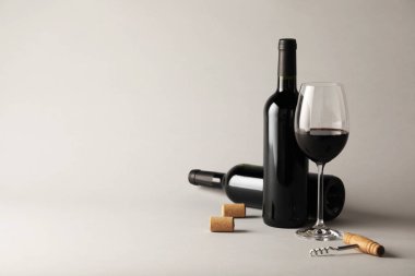 Bardakta kırmızı şarap, şişeler, mantarlar ve açık gri arka planda tirbuşon, metin için yer