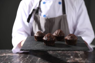 Karanlık masada lezzetli çikolatalı kekleri olan şekerci, yakın plan.