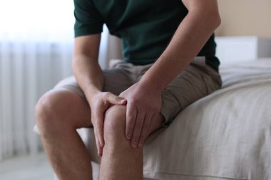 Evdeki yatakta diz ağrısı çeken bir adam, yakın plan.