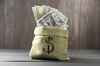 Gri ahşap masanın üzerinde dolar banknotları olan para çantası.