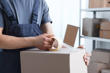Kapalı alanda yapıştırıcı bantlı karton kutu mühürleyen adam.