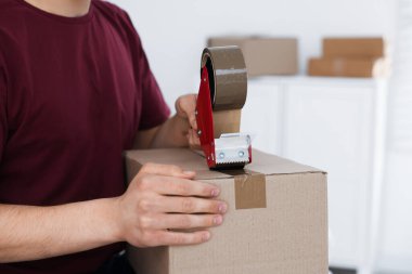 Karton kutuyu kapalı bir yere kapatmak için yapıştırıcılı bant kullanan bir adam.