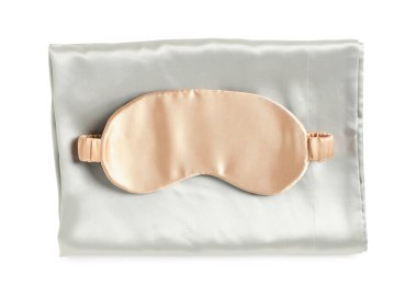 Beyaz arka planda ipek çarşaflar ve uyku maskesi, üst manzara.