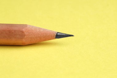 Sarı arka planda keskin bir grafit kalem, yakın plan.
