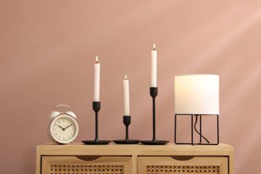 Mumları yanan şamdanlar, çalar saat ve lamba açık kahverengi duvarın yanındaki ahşap dolapta.