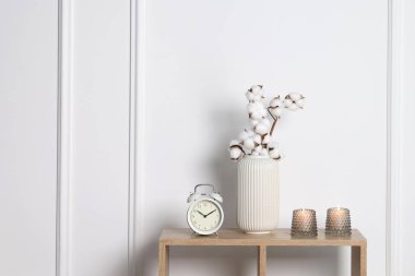 Mumları yanan şamdanlar, çalar saat ve vazolardan oluşan pamuk dallar beyaz duvarın yanındaki ahşap masada, yazı için yer var.