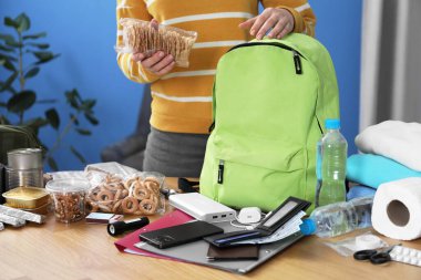 Hayatta kalma kiti. Kadın, ahşap masada sırt çantasına farklı acil durum malzemeleri yerleştiriyor.