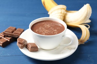 Lezzetli çikolatalı süt, parçalar ve muz mavi ahşap masada, yakın plan.