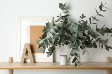 Vazodaki okaliptüs dalları ve beyaz duvarın yanındaki ahşap masa üzerindeki diğer dekorlar.