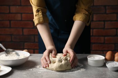 Açık gri masada hamur yoğuran kadın, yakın plan.