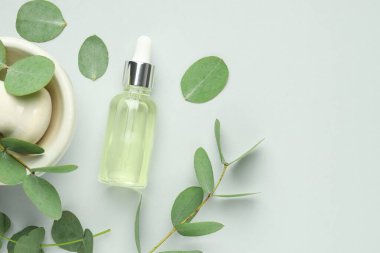 Bir şişe temel yağ, okaliptüs yaprakları, beyaz arka planda havan ve tokmak, düz bir zemin. Metin için boşluk