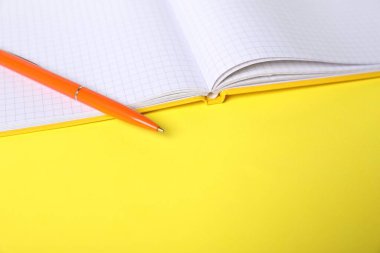 Sarı arka planda kalem ve açık defter, yakın plan. Metin için boşluk